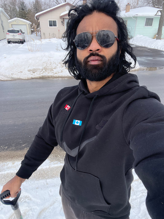 Man wearing sunglasses and a black hoodie with logos, standing on a snowy street.