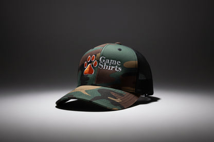 Camouflage baseball cap with paw print and 'Game Shirts' logo on grass