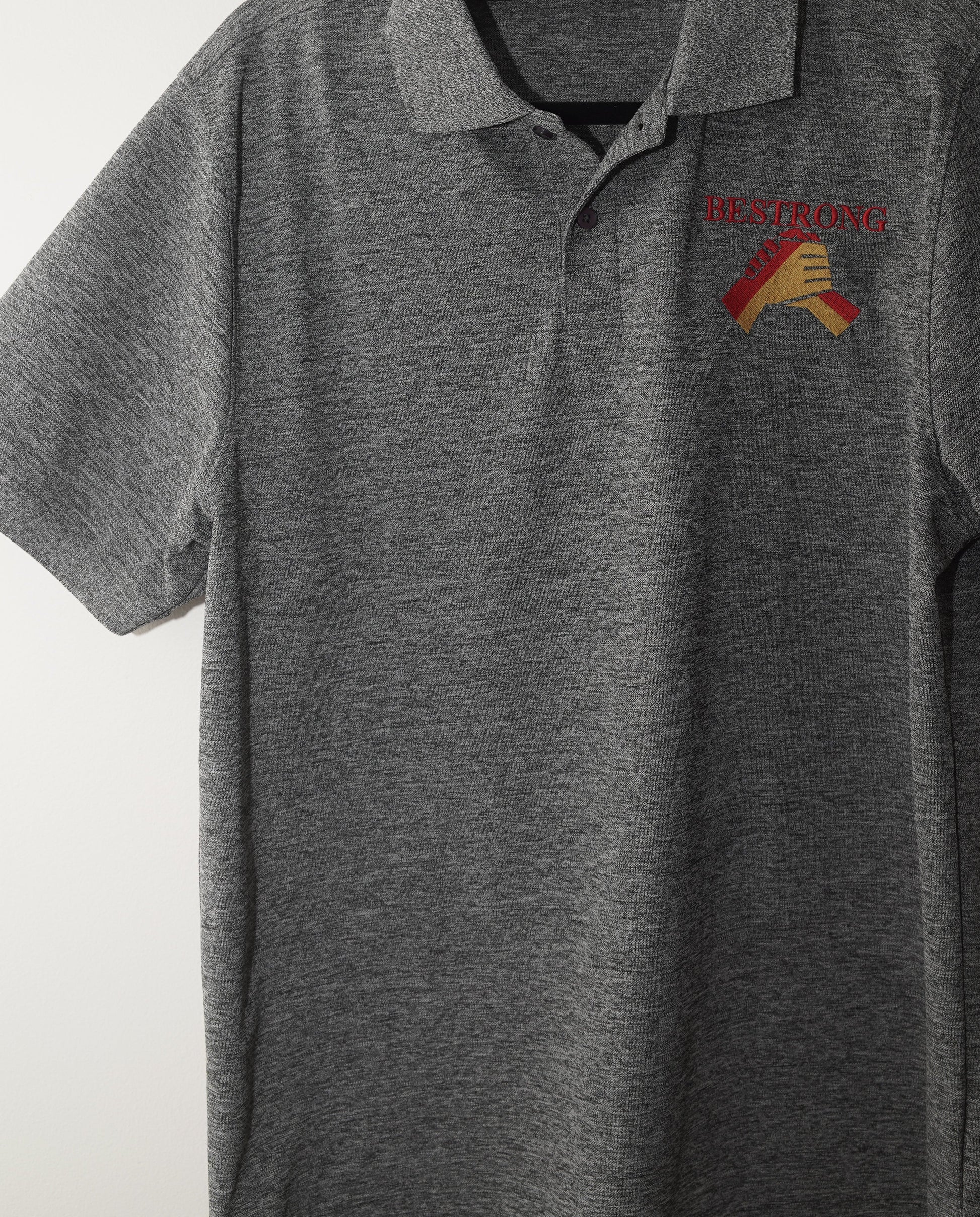 A gray heathered long-sleeve polo shirt with a small embroidered logo on the left chest, hanging on a white wall.