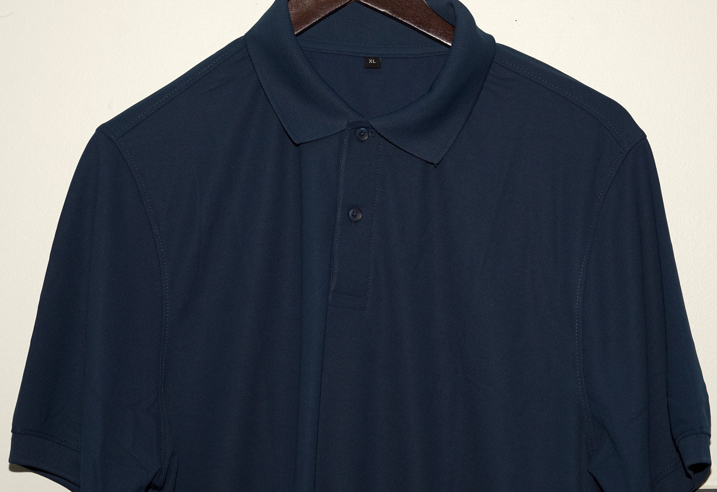Navy blue polo shirt on a hanger against a beige background
