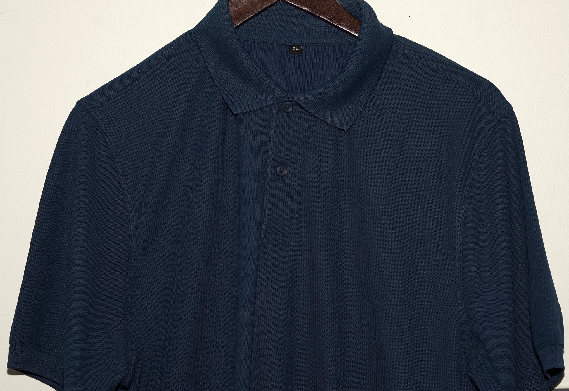 Navy blue polo shirt on a hanger against a beige background