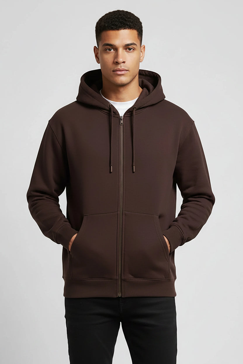 A man wearing a dark brown pullover hoodie with black drawstrings and a front kangaroo pocket, paired with black pants, against a light gray studio background.